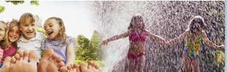 Girls smiling in yard; children running through a sprinkler